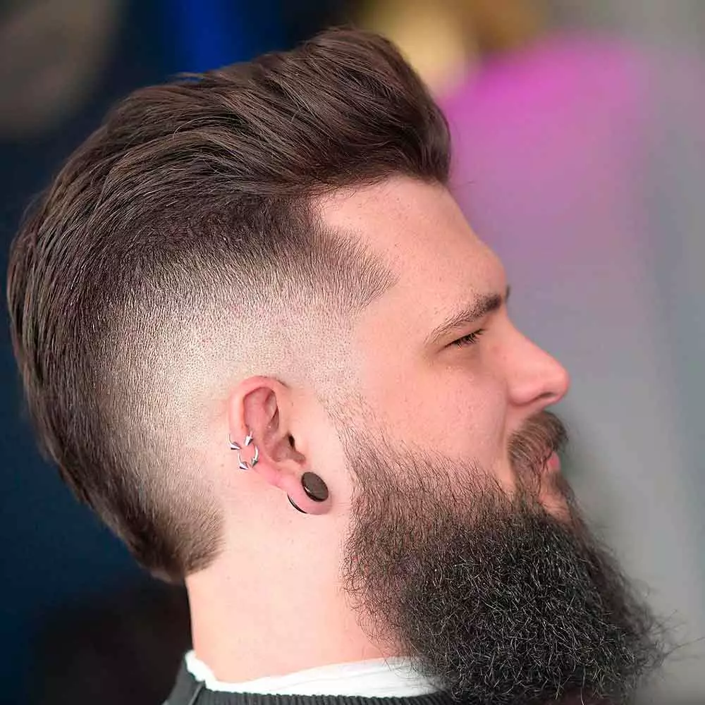 High burst fade with straight hair styled in a sleek comb-over with clean curved fade around the ear for a modern look.