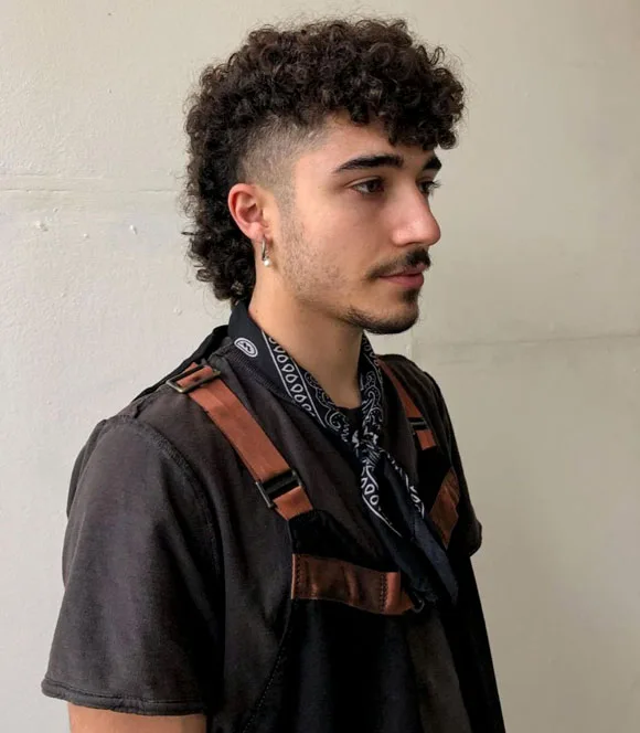 Man with short sides and long curly mullet haircut styled in modern barber shop.